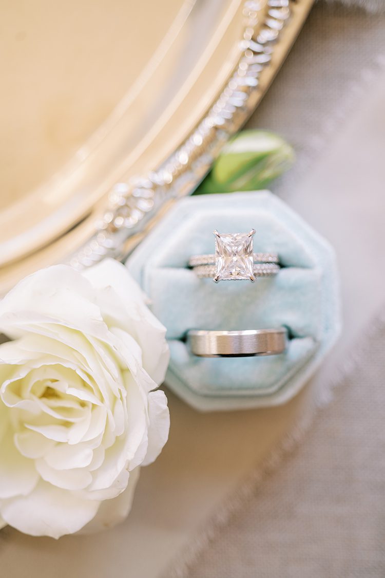 Bride's cushion cut engagement ring with diamond eternity wedding band accompany by Groom's silver wedding band in blue velvet ring box, planned by Outer Banks Wedding Planner, Jenna Nichols of Better2gether Events